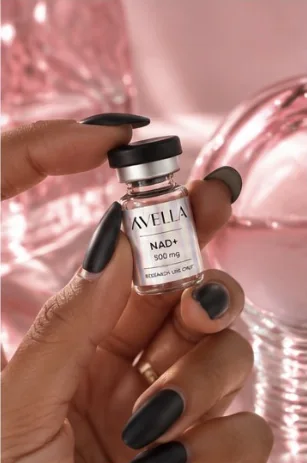 Hand holding an AVELLA NAD+ 500 mg vial against pink satin